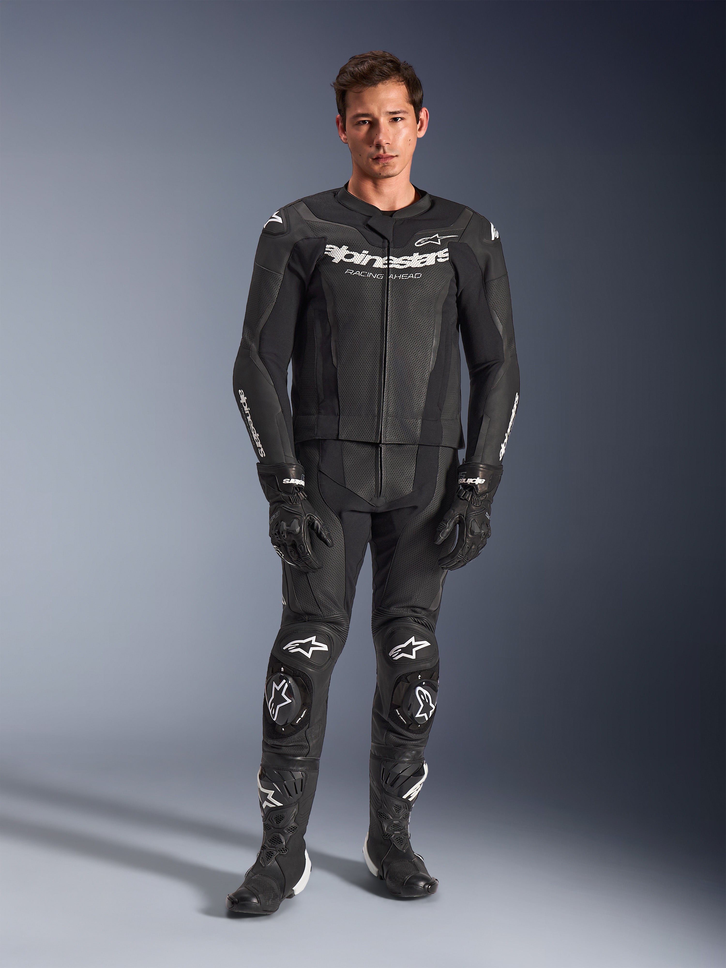 Alpinestars GP Force V2 Leather Suit 2-Piece, negro con logotipos blancos, mono de competición integral para motociclismo, con construcción de cuero de primera calidad, deslizadores de rodilla reforzados y paneles perforados, combinado con guantes y botas negros, vista de estudio de cuerpo completo