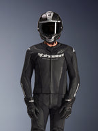 Piloto con traje de cuero de 2 piezas Alpinestars GP Force V2 en color negro, construcción de cuero perforado con logotipo 'Racing Ahead' blanco en el pecho, casco integral plateado y de fibra de carbono, guantes negros, equipamiento profesional para conducción deportiva y en pista