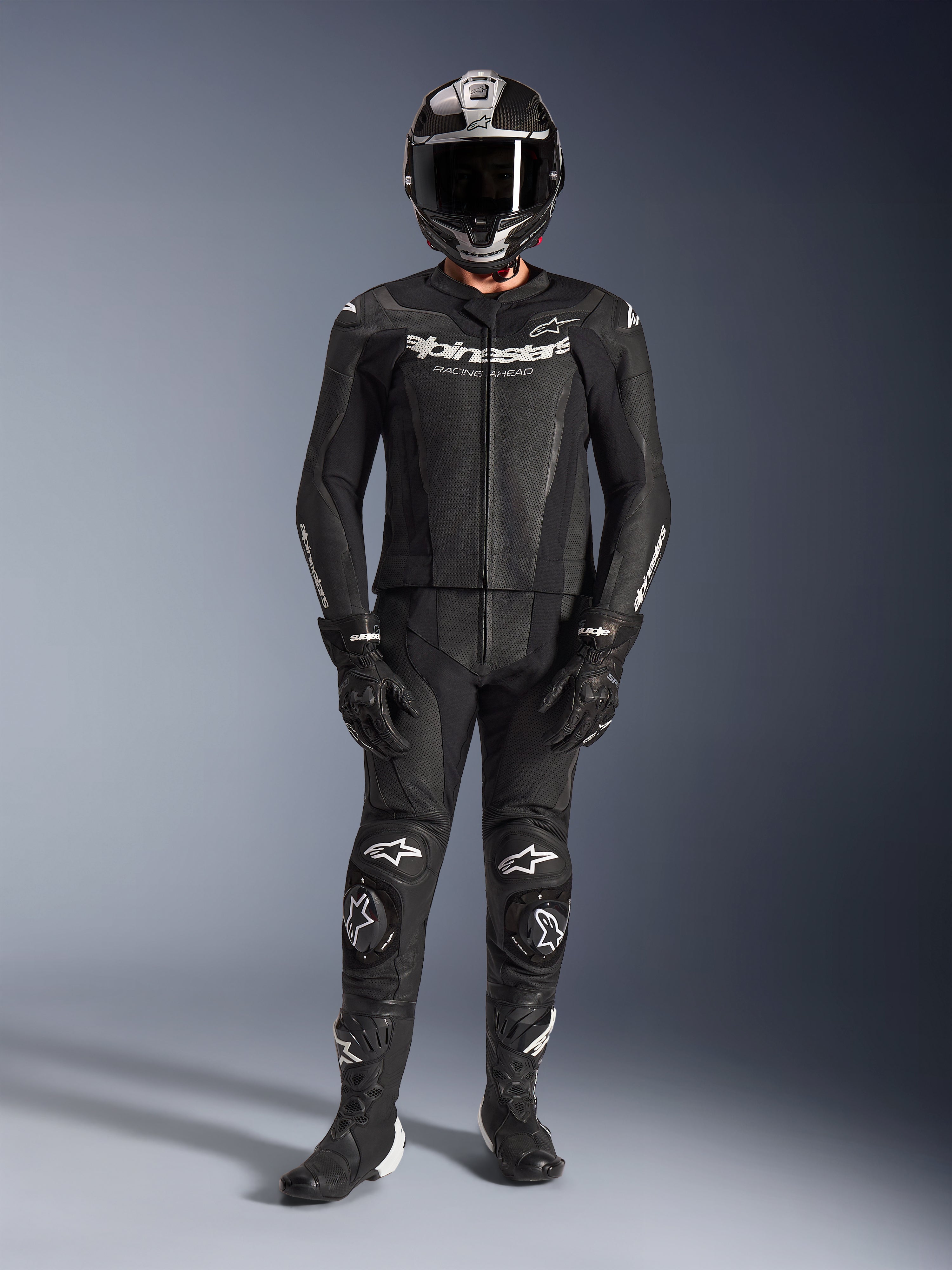 Traje de cuero de 2 piezas Alpinestars GP Force V2, negro, equipo integral de competición que incluye casco, guantes y botas negras, con paneles de cuero perforado y logotipos blancos de Alpinestars en el pecho y las rodillas, diseñado para conducción de alto rendimiento en pista.