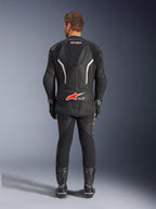 Vista trasera de un piloto con el traje de cuero de 2 piezas Alpinestars GP Force V2, negro con detalles en blanco y rojo, con logotipos prominentes de Alpinestars y Tech-Air Ready en la espalda, combinado con guantes y botas de carreras negros a juego.
