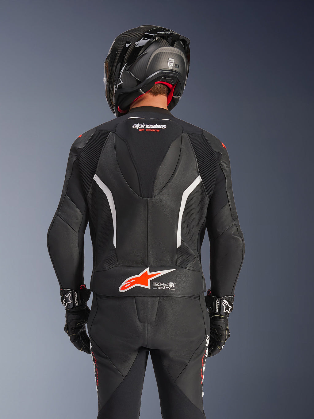 Vista trasera del traje de cuero de 2 piezas Alpinestars GP Force V2 en color negro, con cuero perforado, detalles en blanco y el logotipo de Alpinestars en rojo en la parte inferior de la espalda, usado con un casco de moto negro y guantes de carreras.