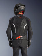 Vista trasera del traje de cuero de 2 piezas Alpinestars GP Force V2 en color negro, con cuero perforado, detalles en blanco y el logotipo de Alpinestars en rojo en la parte inferior de la espalda, usado con un casco de moto negro y guantes de carreras.
