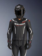 Traje de cuero de 2 piezas Alpinestars GP Force V2, en negro, blanco y rojo flúor, usado por un piloto con casco integral de fibra de carbono y guantes de carreras negros, con paneles de cuero perforado y el logotipo de Alpinestars en el pecho.