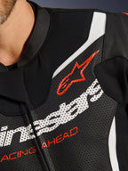Traje de cuero de 2 piezas Alpinestars GP Force V2, primer plano del pecho, cuero negro perforado con acentos blancos y rojos, con el logotipo rojo de Alpinestars y el texto 'RACING AHEAD', detalle de equipamiento premium para motociclismo de competición