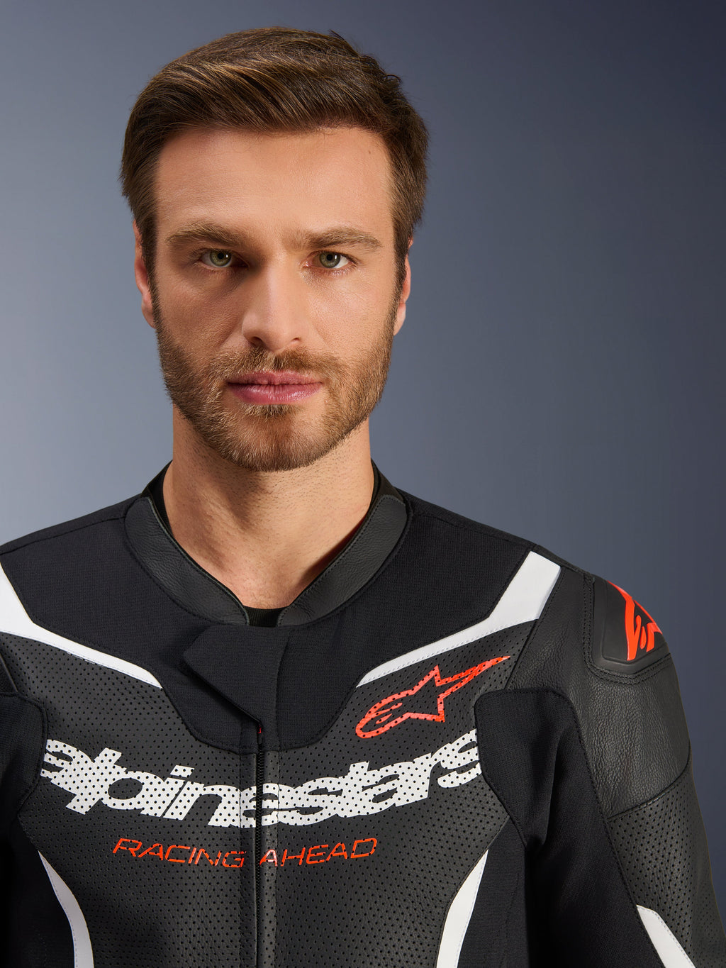 Chaqueta del traje de cuero de dos piezas Alpinestars GP Force V2, negro, blanco y rojo flúor, retrato de primer plano con cuero perforado, logotipo de Alpinestars en blanco y texto 'RACING AHEAD' en rojo, equipamiento de motociclismo de alto rendimiento