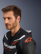 Alpinestars GP Force V2 Leather Suit 2-Piece, primer plano de la chaqueta usada por un modelo masculino, negro, blanco y rojo flúor, con cuero perforado, logotipo de estrella roja en el hombro, joroba aerodinámica y marca Alpinestars en el pecho, equipamiento profesional de carreras de motos