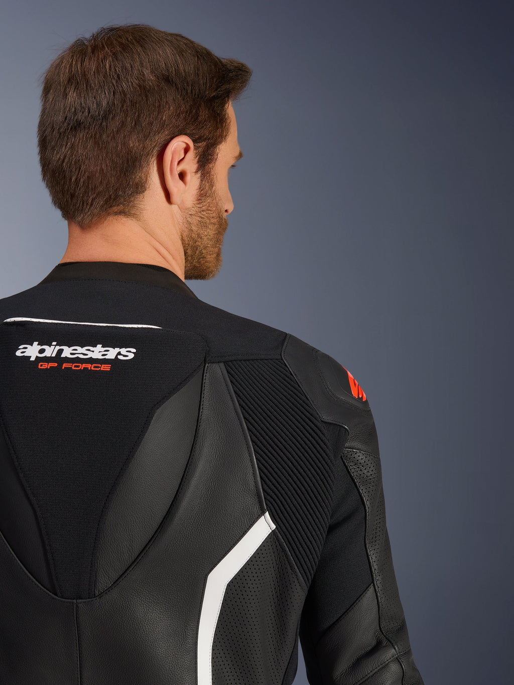 Traje de cuero de 2 piezas GP Force V2 de Alpinestars, primer plano de la parte superior de la espalda y el hombro en un modelo masculino, cuero negro con detalles en blanco y rojo, marca Alpinestars GP Force, con paneles perforados y zonas elásticas de acordeón para competición.
