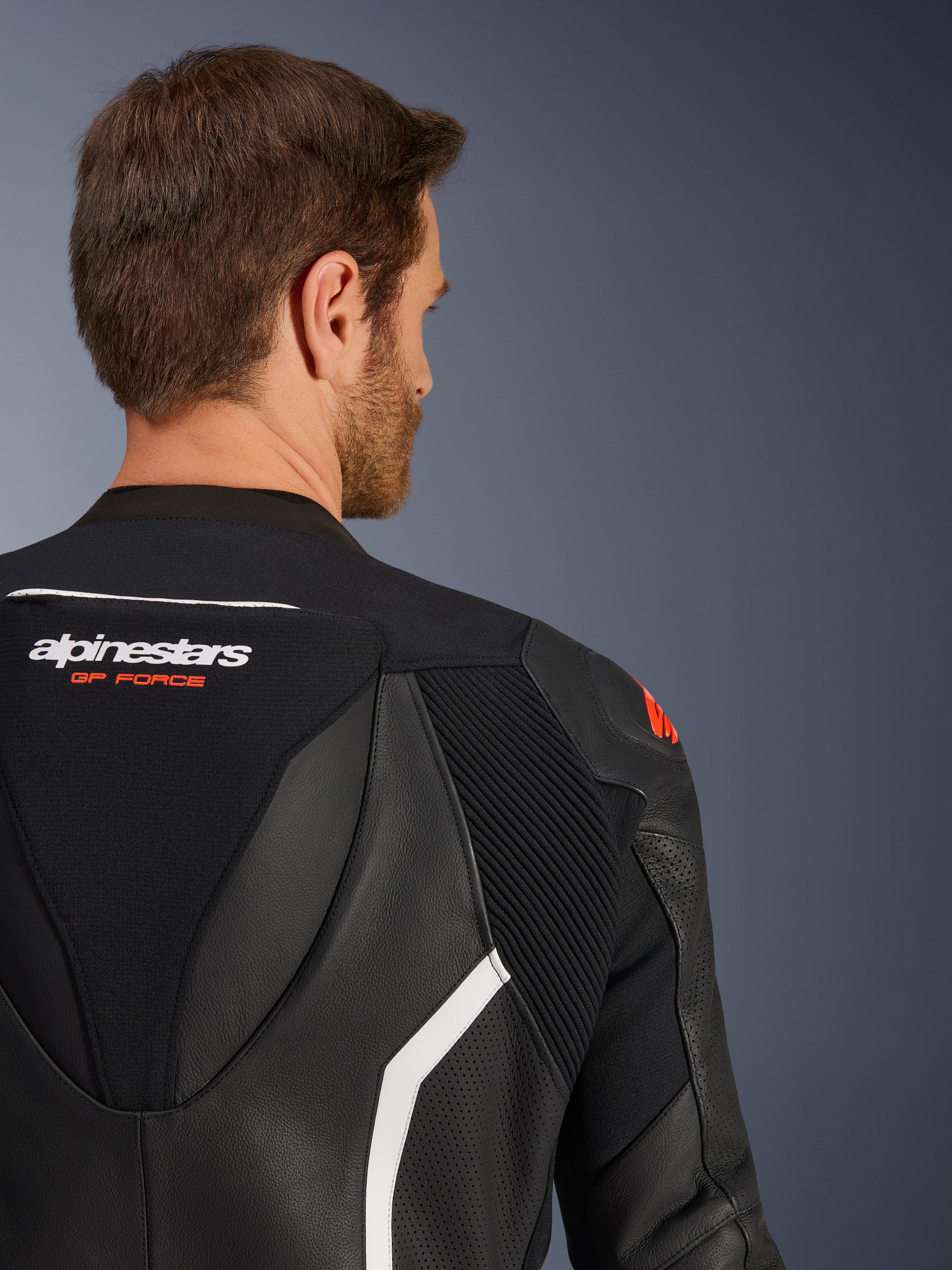 Traje de cuero de 2 piezas GP Force V2 de Alpinestars, primer plano de la parte superior de la espalda y el hombro en un modelo masculino, cuero negro con detalles en blanco y rojo, marca Alpinestars GP Force, con paneles perforados y zonas elásticas de acordeón para competición.