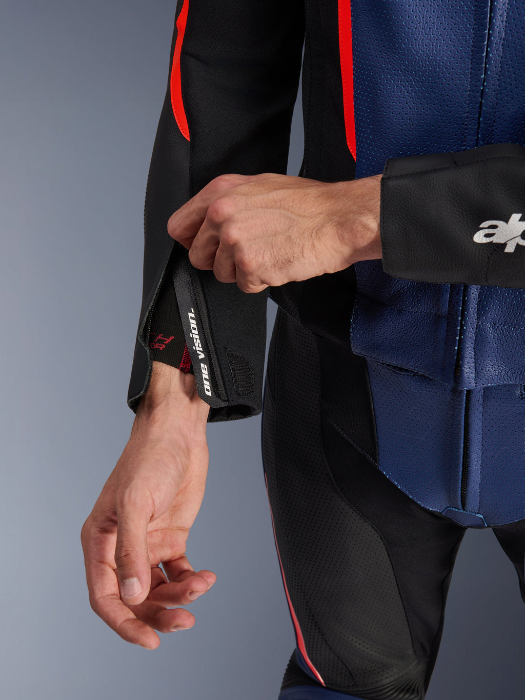 Traje de cuero de 2 piezas Alpinestars GP Force V2, detalle de primer plano del puño de la manga y el torso, negro, azul y rojo flúor, con cuero perforado, cremallera en la muñeca con la marca 'one vision' y detalles en rojo flúor, equipamiento profesional para conducción deportiva