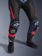 Mono de cuero Alpinestars GP Force V2 de 2 piezas, traje de carreras de moto, negro, azul y rojo flúor, con cuero perforado, paneles de rodilla en acordeón con deslizadores protectores y logotipo de Alpinestars, combinado con botas de carreras negras