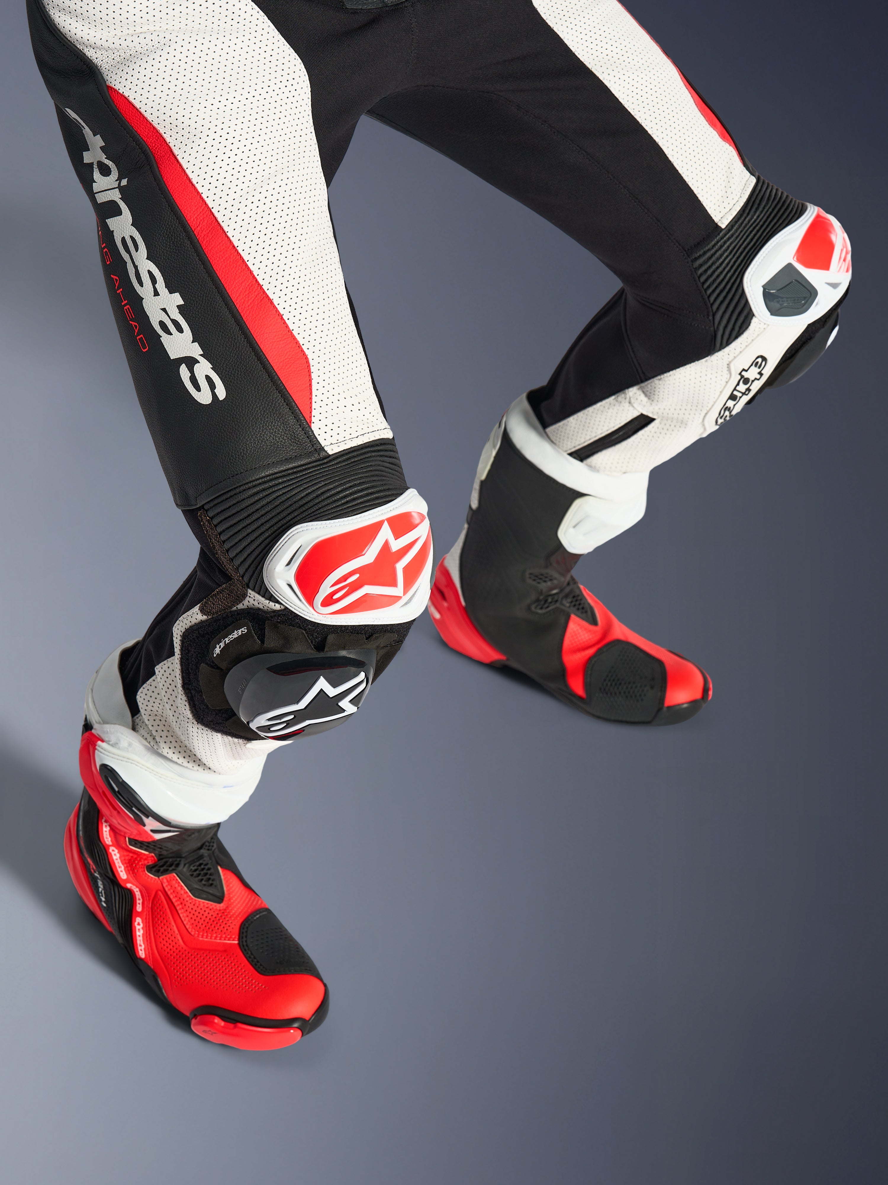Alpinestars Stella GP-R7 Traje de Cuero de 2 Piezas para mujer, parte inferior de las piernas y botas de carrera, Negro Blanco y Rojo Fluo, con cuero perforado, logotipo de Alpinestars en el muslo, paneles elásticos de acordeón y deslizadores de rodilla rojos y blancos con botas técnicas rojas y negras a juego.