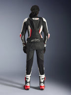 Vista posterior del traje de cuero de 2 piezas Alpinestars Stella GP-R7, negro, blanco y rojo flúor, con una joroba aerodinámica con marca GP-R7 y logotipo Tech-Air Ready, usado con botas y guantes de carreras a juego, equipamiento profesional de motociclismo para mujer