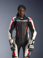 Modelo femenina con el traje de cuero Alpinestars Stella GP-R7 de 2 piezas en negro, blanco y rojo flúor, con paneles de cuero perforados y guantes GP Pro a juego, optimizado anatómicamente para mujeres.
