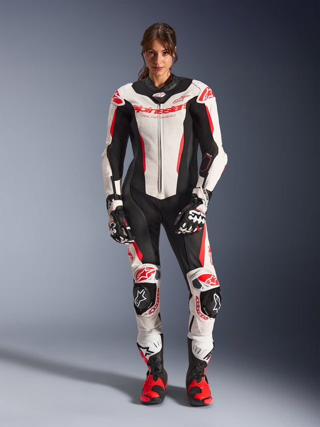 Piloto mujer con mono de cuero de una pieza Alpinestars Stella GP-R7 en blanco, negro y rojo flúor, equipamiento de motociclismo para competición con paneles de cuero perforado y protecciones integradas, combinado con guantes y botas de carreras a juego
