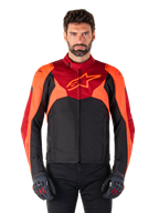 Alpinestars T-Jaws V4 Waterproof Jacket, chaqueta textil de moto deportiva, negra con detalles en rojo flúor y rojo oscuro, lucida por un modelo masculino con guantes a juego, equipamiento técnico con un destacado logotipo de estrella en el pecho.