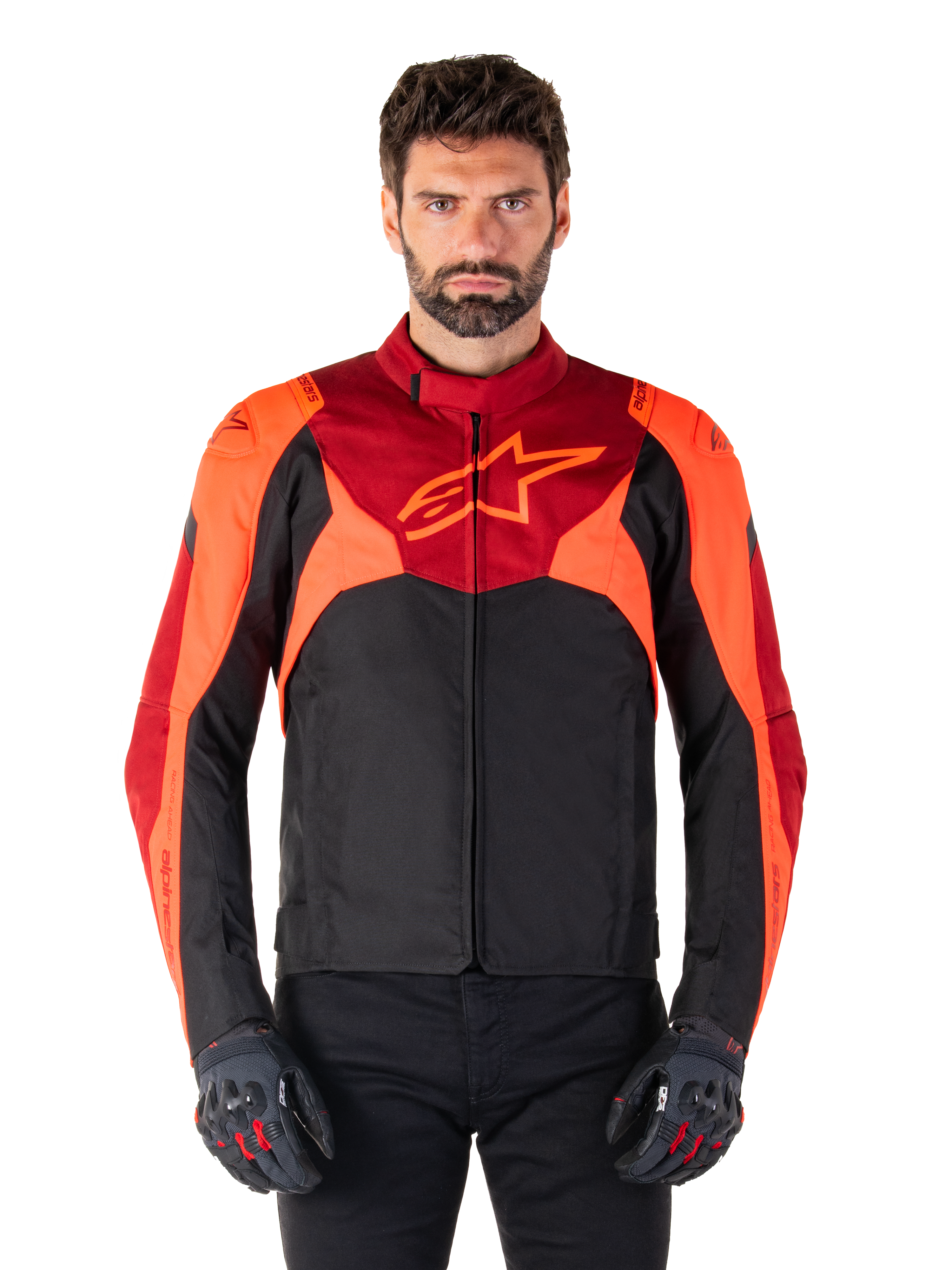 Alpinestars T-Jaws V4 Waterproof Jacket, chaqueta textil de moto deportiva, negra con detalles en rojo flúor y rojo oscuro, lucida por un modelo masculino con guantes a juego, equipamiento técnico con un destacado logotipo de estrella en el pecho.