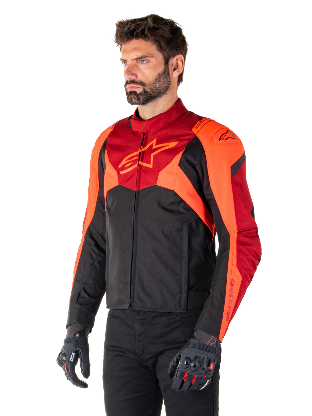 Chaqueta Alpinestars T-Jaws V4 Waterproof, negro, rojo flúor y rojo oscuro, usada por un modelo masculino con pantalones negros y guantes de moto, silueta deportiva agresiva con el logo de Alpinestars en el pecho, vista de tres cuartos