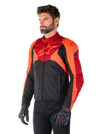 Chaqueta Alpinestars T-Jaws V4 Waterproof, negro, rojo flúor y rojo oscuro, usada por un modelo masculino con pantalones negros y guantes de moto, silueta deportiva agresiva con el logo de Alpinestars en el pecho, vista de tres cuartos