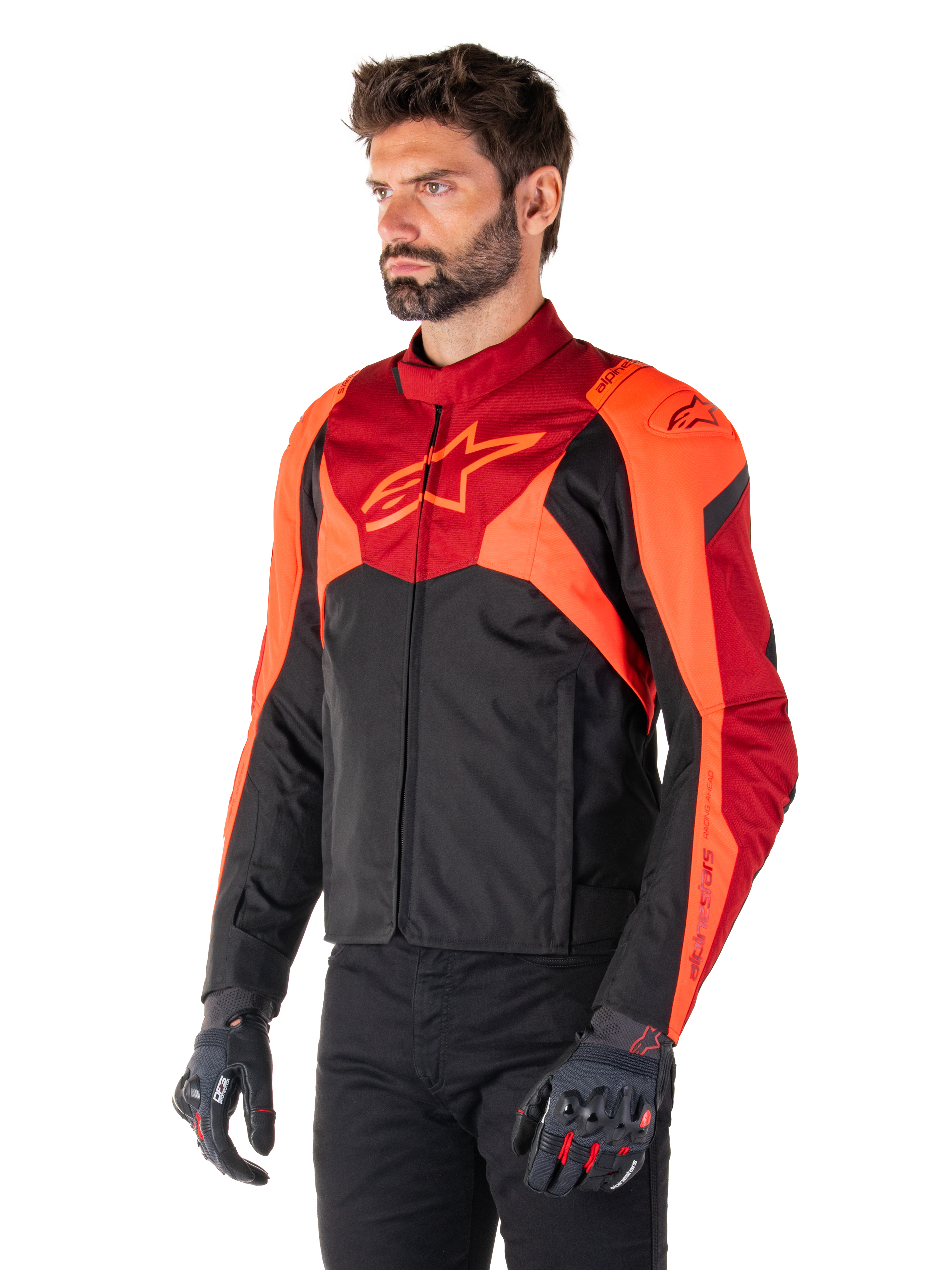 Chaqueta Alpinestars T-Jaws V4 Waterproof, negro, rojo flúor y rojo oscuro, usada por un modelo masculino con pantalones negros y guantes de moto, silueta deportiva agresiva con el logo de Alpinestars en el pecho, vista de tres cuartos