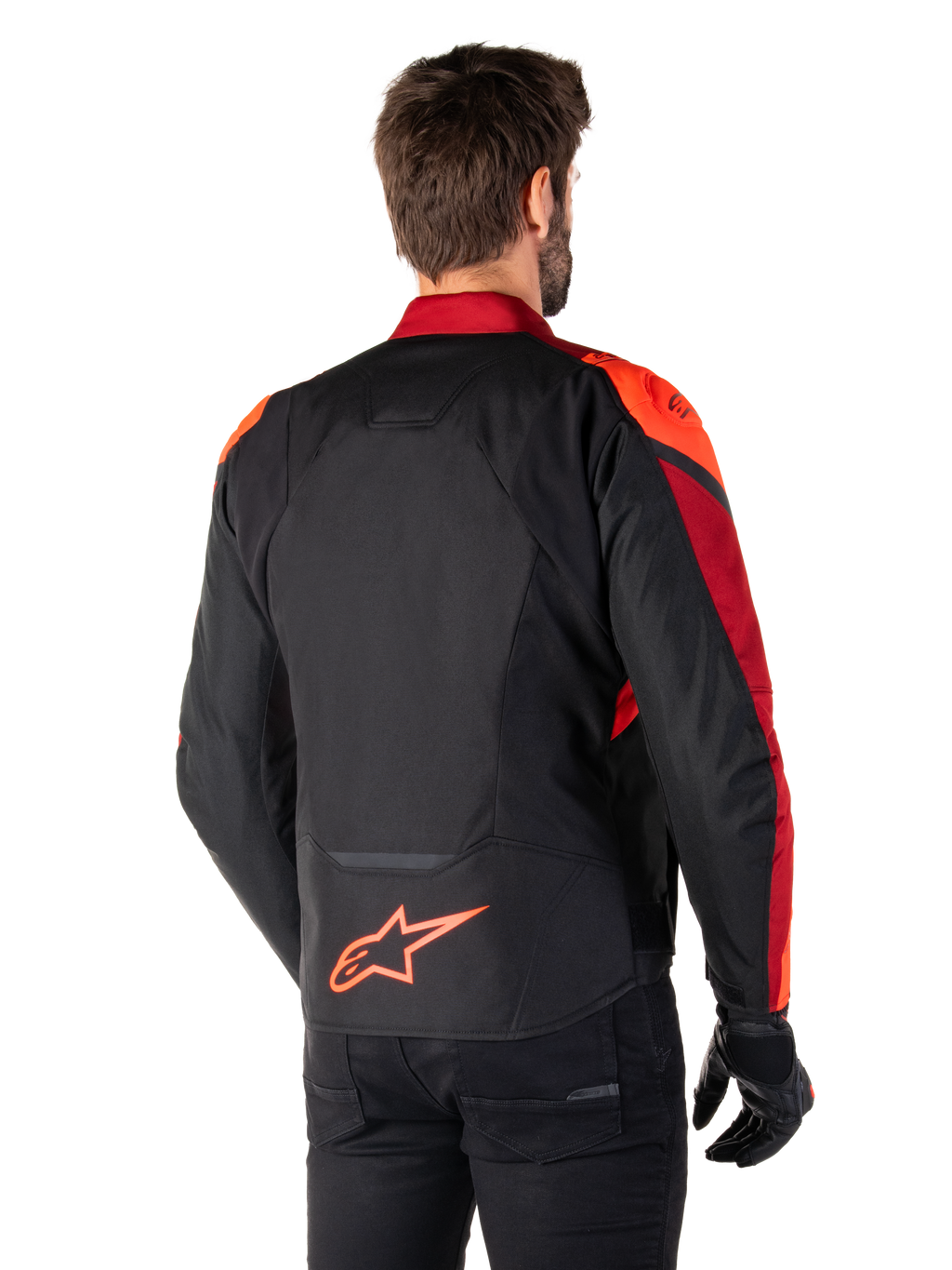 Vista trasera de un hombre con la chaqueta Alpinestars T-Jaws V4 Waterproof en Negro Rojo Fluo Rojo Oscuro, con detalles en rojo vibrante en hombros y mangas, logotipo de Alpinestars en rojo flúor en la parte inferior de la espalda, combinada con pantalones y guantes negros.