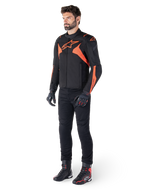 Alpinestars T-Jaws V4 Waterproof Jacket, Black and Red Fluo, worn by a male model with black pants, gloves, and boots, featuring bright orange accents and the Alpinestars logo, sporty design for motorcycle riding
