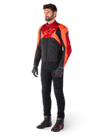 Piloto con la chaqueta Alpinestars T-Jaws V4 Waterproof en color negro, rojo flúor y rojo oscuro, combinada con pantalones de moto, guantes y botas de conducción negros, con un diseño textil de ajuste deportivo, logotipo llamativo en el pecho y una silueta agresiva.
