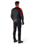Chaqueta Alpinestars T-Jaws V4 Waterproof en color negro, rojo flúor y rojo oscuro, vista trasera de un piloto con la chaqueta textil, pantalones negros y botas de moto, con un llamativo logotipo rojo de Alpinestars en la parte inferior de la espalda.
