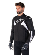 Chaqueta impermeable Alpinestars T-Jaws V4, en negro y blanco, lucida por un modelo con guantes de moto, con destacados logos y detalles de Alpinestars en blanco, chaqueta de moto textil con ajuste deportivo para carretera