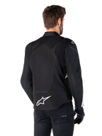 Chaqueta impermeable Alpinestars T-Jaws V4, negro y blanco, vista trasera, chaqueta textil deportiva para moto con logotipo blanco en la parte inferior de la espalda, combinada con guantes y pantalones negros, con una silueta de ajuste deportivo renovada