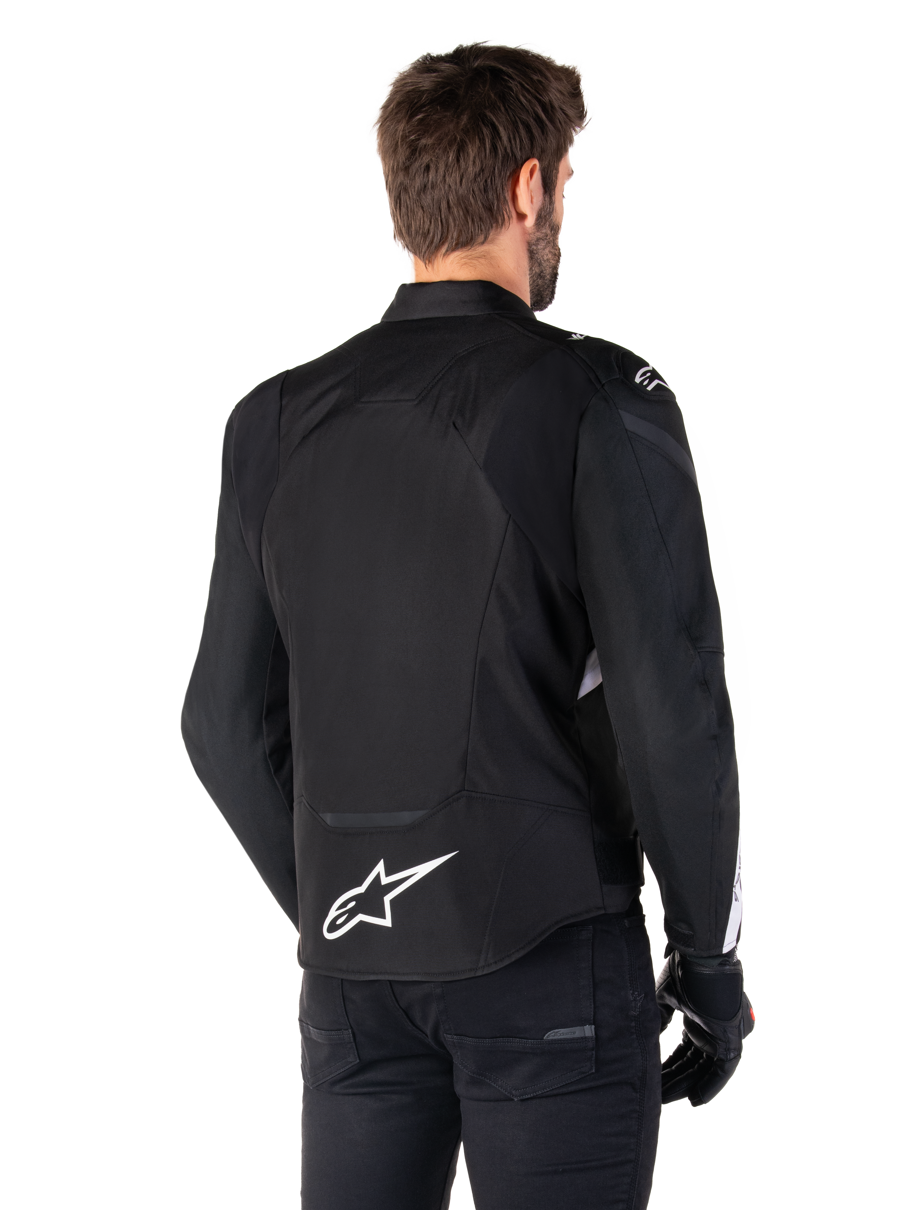 Chaqueta impermeable Alpinestars T-Jaws V4, negro y blanco, vista trasera, chaqueta textil deportiva para moto con logotipo blanco en la parte inferior de la espalda, combinada con guantes y pantalones negros, con una silueta de ajuste deportivo renovada