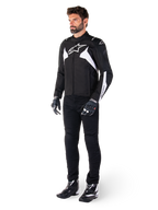 Chaqueta impermeable Alpinestars T-Jaws V4 en color negro y blanco, modelo masculino con chaqueta textil deportiva que incluye el logotipo de la estrella en blanco y detalles en las mangas, combinada con pantalones, guantes y botas de moto negros para un look completo de carretera.