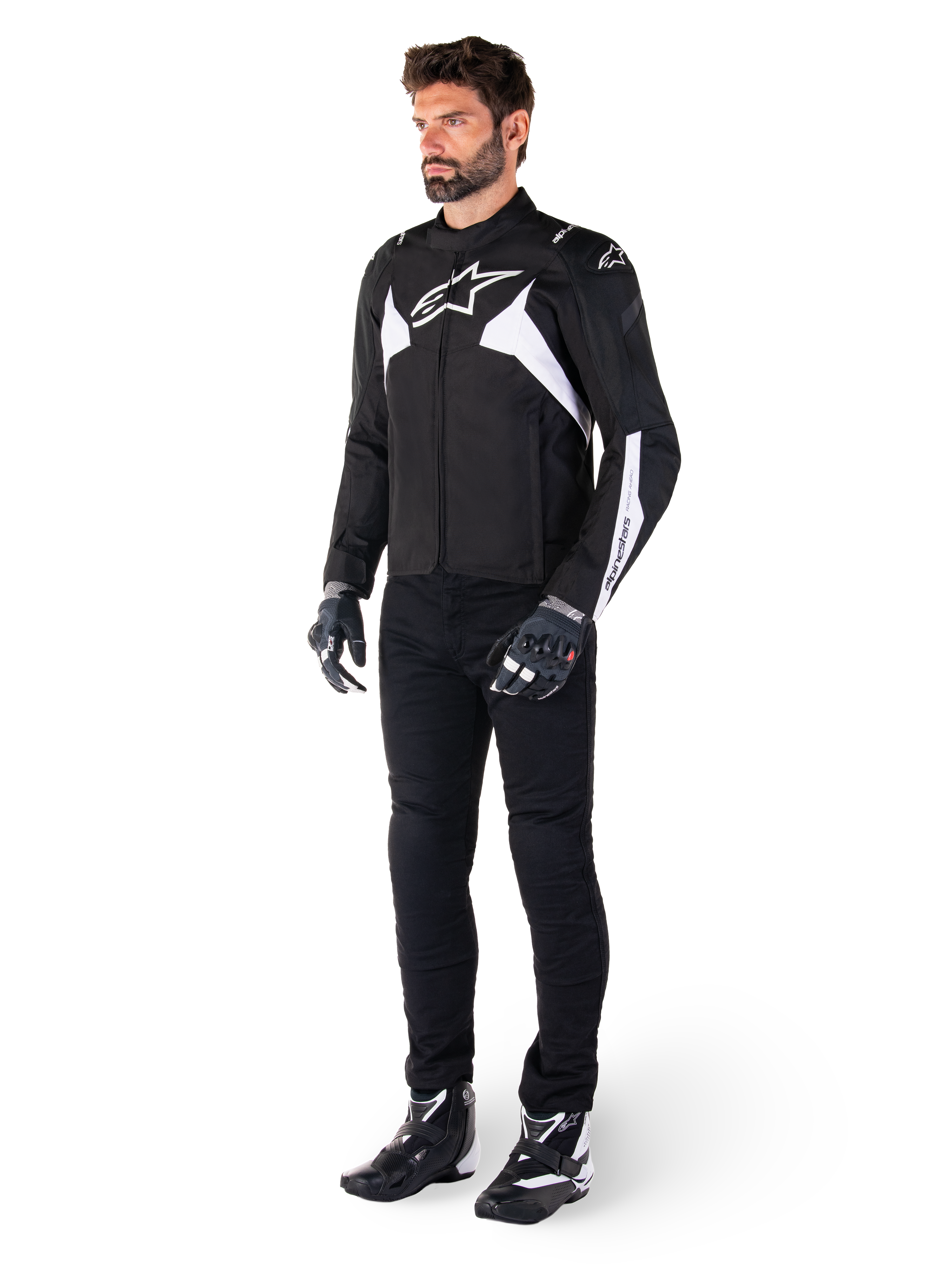 Chaqueta impermeable Alpinestars T-Jaws V4 en color negro y blanco, modelo masculino con chaqueta textil deportiva que incluye el logotipo de la estrella en blanco y detalles en las mangas, combinada con pantalones, guantes y botas de moto negros para un look completo de carretera.