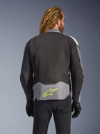 Alpinestars T-Jaws V4 Waterproof Jacket, Black Ice Gray Dark Gray, rear view on model, featuring a light gray lower back panel with a prominent neon yellow star logo, multi-panel textile construction, and a sporty silhouette, worn with black gloves and dark pants.
