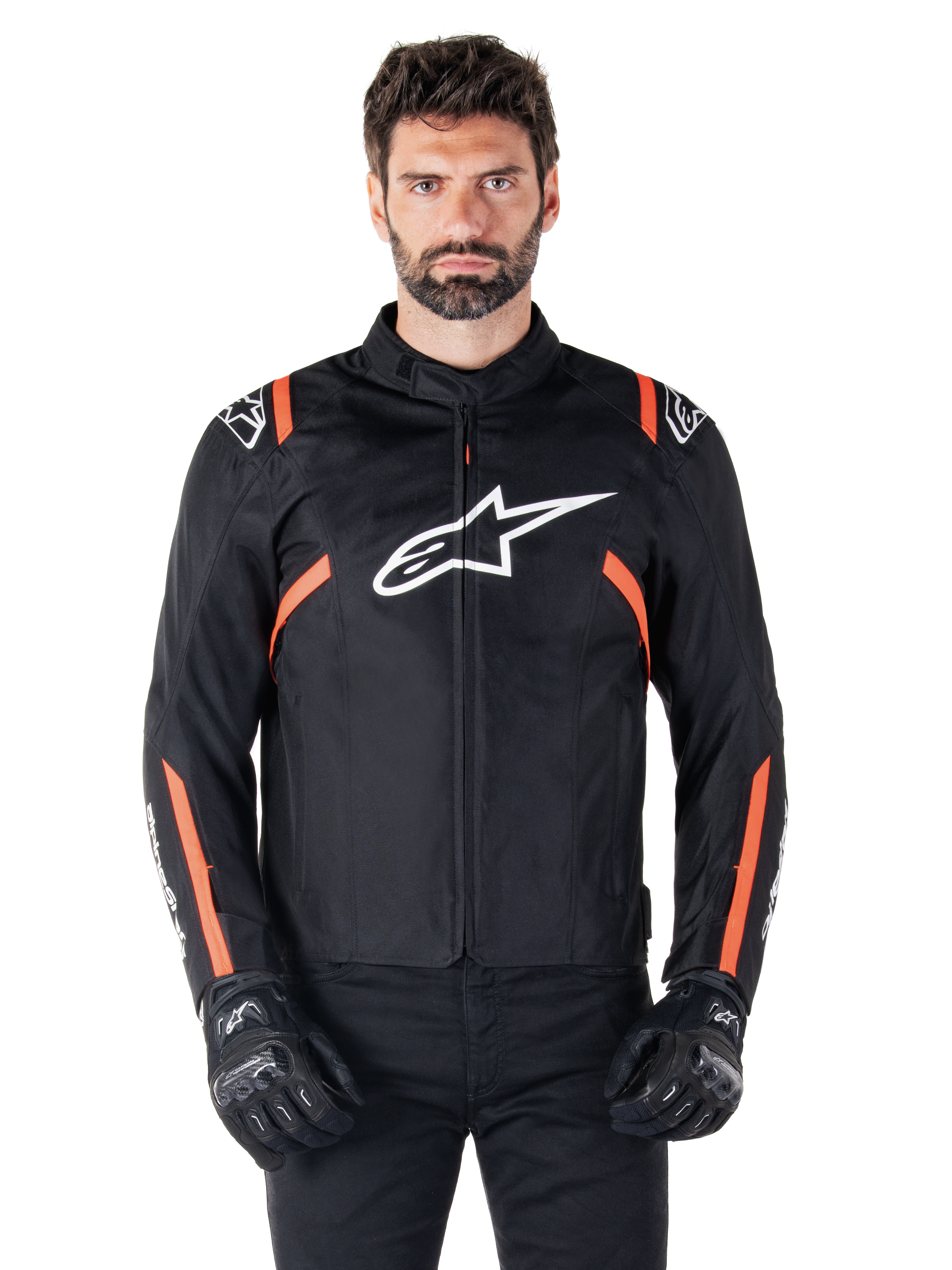 Alpinestars T-SPS V2 Waterproof Jacket, chaqueta impermeable en negro, blanco y rojo flúor, lucida por un modelo masculino con guantes de moto negros, con un gran logotipo de Alpinestars en el pecho y llamativos detalles en naranja en los hombros y las mangas
