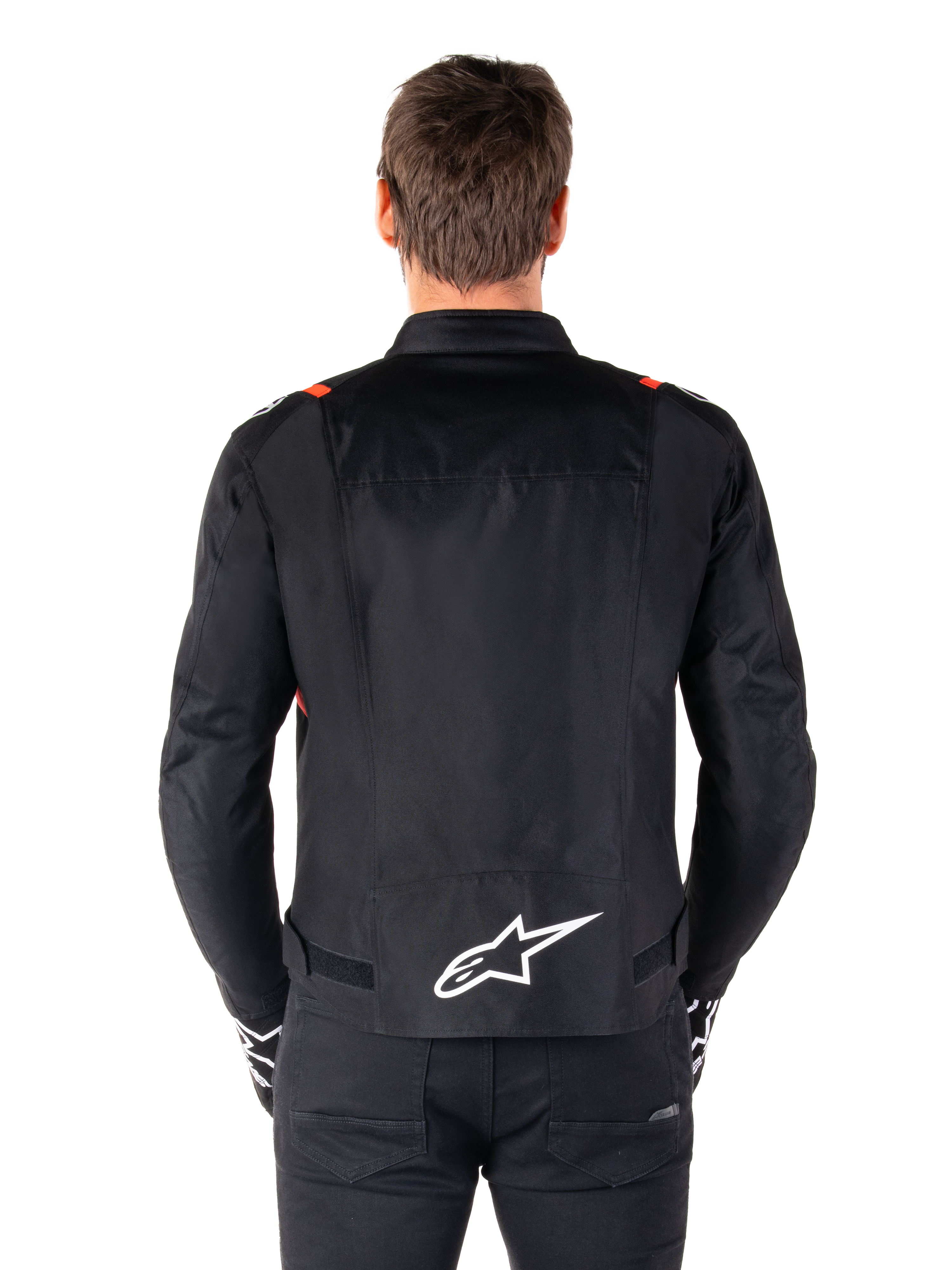Chaqueta impermeable Alpinestars T-SPS V2, negro con detalles en blanco y rojo flúor, vista trasera con un gran logotipo blanco de Alpinestars en la parte inferior de la espalda, chaqueta de moto textil de corte deportivo, combinada con pantalones y guantes negros