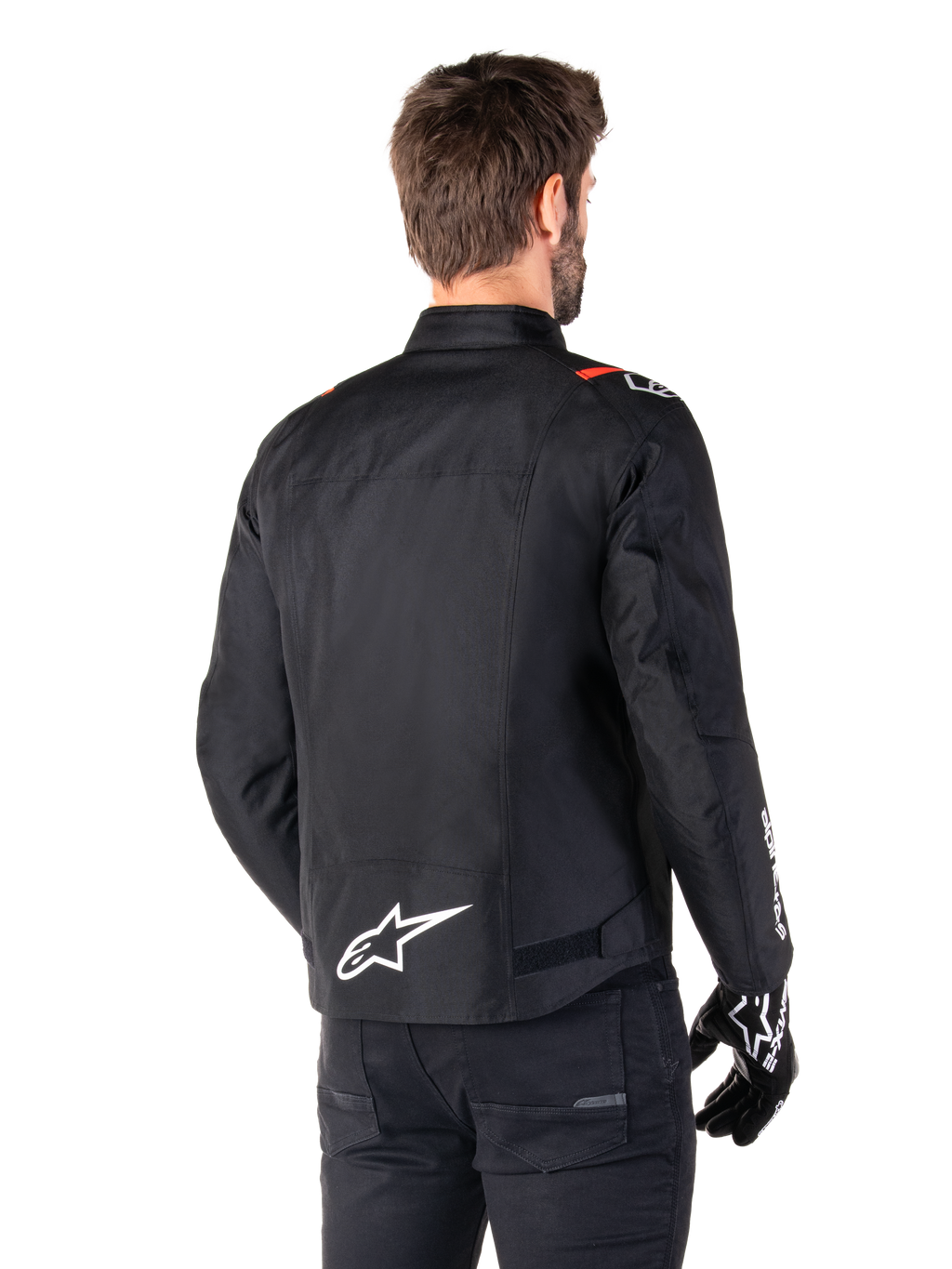 Chaqueta impermeable Alpinestars T-SPS V2, negro, blanco y rojo flúor, vista trasera, con el logotipo blanco de Alpinestars en la parte inferior de la espalda y detalles rojos en los hombros, combinada con guantes y pantalones negros, chaqueta de moto textil de estilo deportivo.
