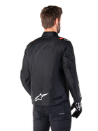 Chaqueta impermeable Alpinestars T-SPS V2, negro, blanco y rojo flúor, vista trasera, con el logotipo blanco de Alpinestars en la parte inferior de la espalda y detalles rojos en los hombros, combinada con guantes y pantalones negros, chaqueta de moto textil de estilo deportivo.