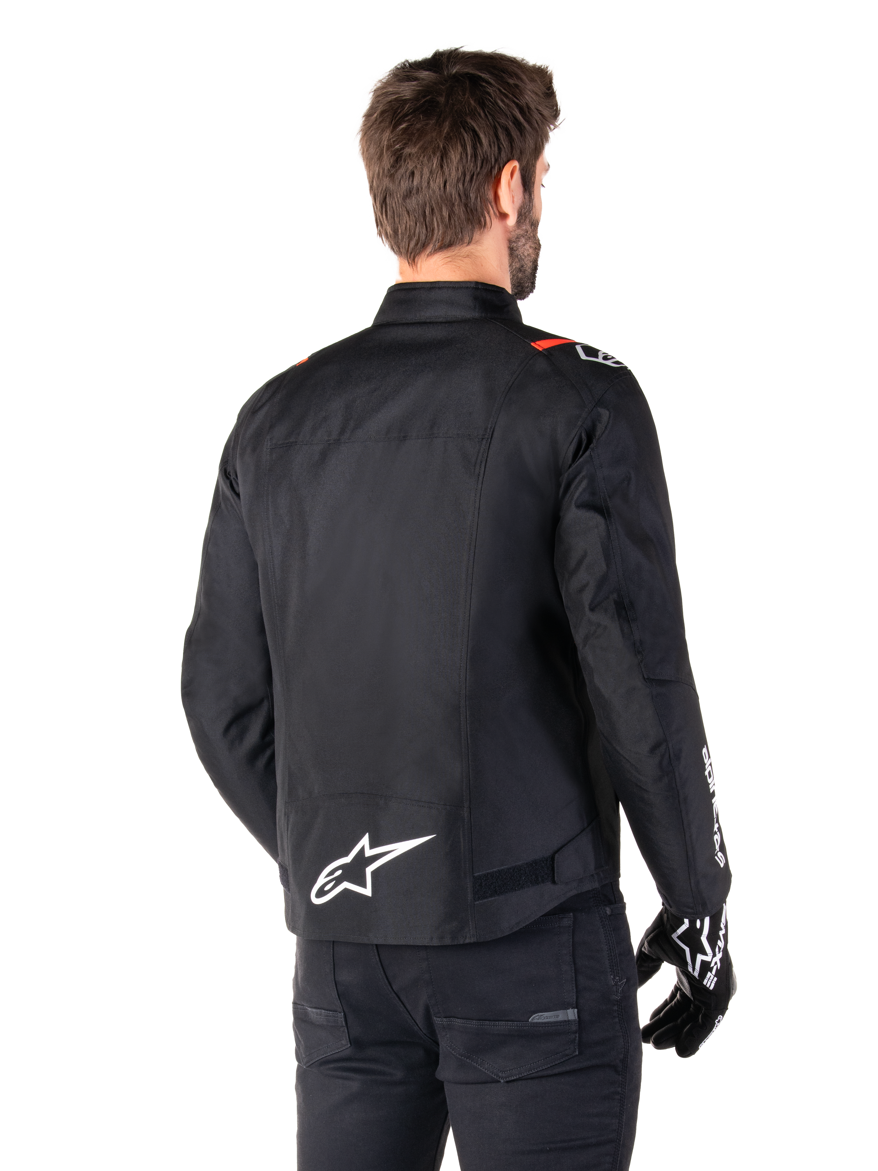 Chaqueta impermeable Alpinestars T-SPS V2, negro, blanco y rojo flúor, vista trasera, con el logotipo blanco de Alpinestars en la parte inferior de la espalda y detalles rojos en los hombros, combinada con guantes y pantalones negros, chaqueta de moto textil de estilo deportivo.