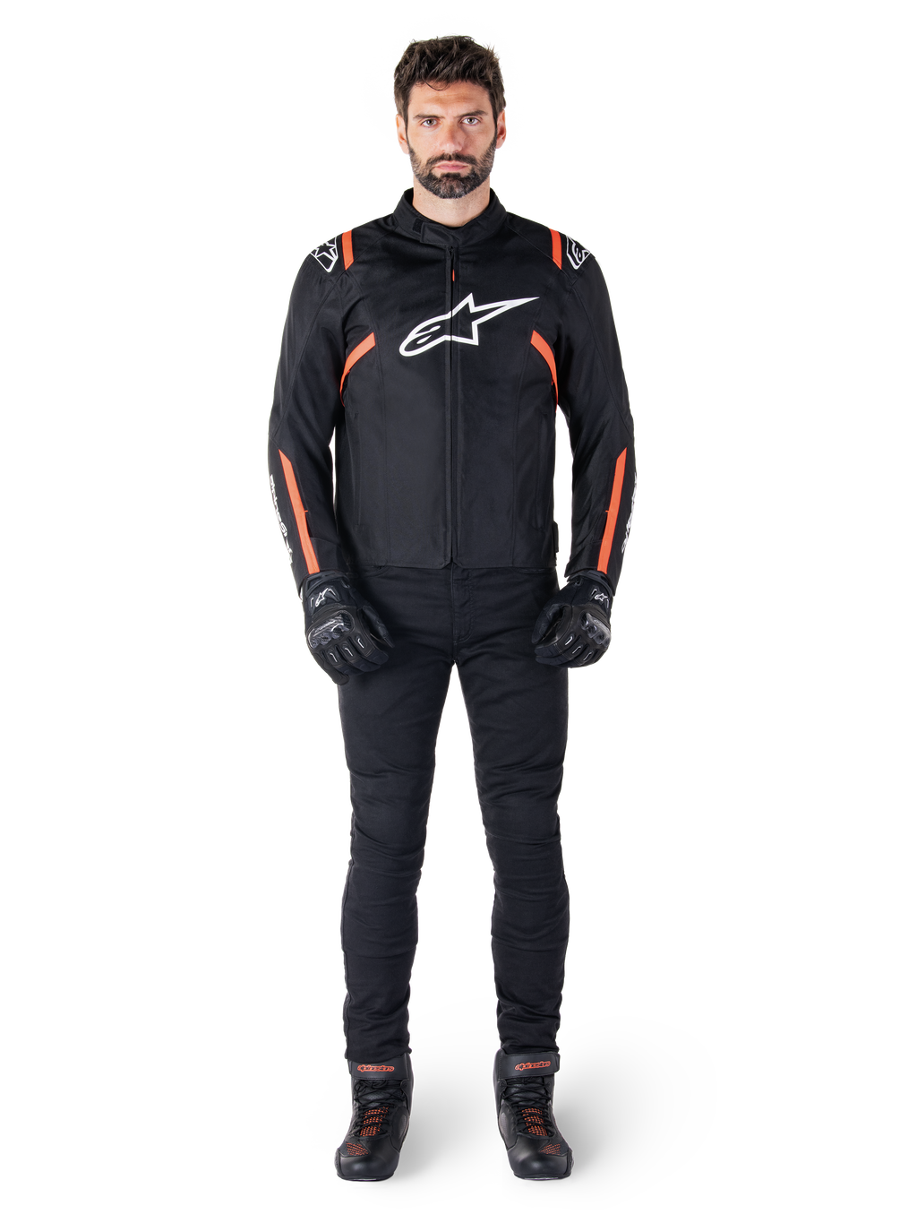 Modelo masculino con la chaqueta impermeable Alpinestars T-SPS V2 en color negro, blanco y rojo flúor, combinada con pantalones y guantes de moto negros, con logotipo de Alpinestars blanco en el pecho y detalles rojos en las mangas