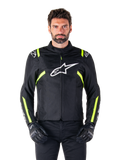 Alpinestars T-SPS V2 Waterproof Jacket, chaqueta de moto, negra con detalles en blanco y amarillo flúor, usada por un modelo con guantes negros, con el logo de la estrella blanca en el pecho y franjas amarillo neón en las mangas y hombros, equipamiento textil deportivo para cualquier clima