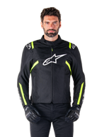 Alpinestars T-SPS V2 Waterproof Jacket, chaqueta de moto, negra con detalles en blanco y amarillo flúor, usada por un modelo con guantes negros, con el logo de la estrella blanca en el pecho y franjas amarillo neón en las mangas y hombros, equipamiento textil deportivo para cualquier clima