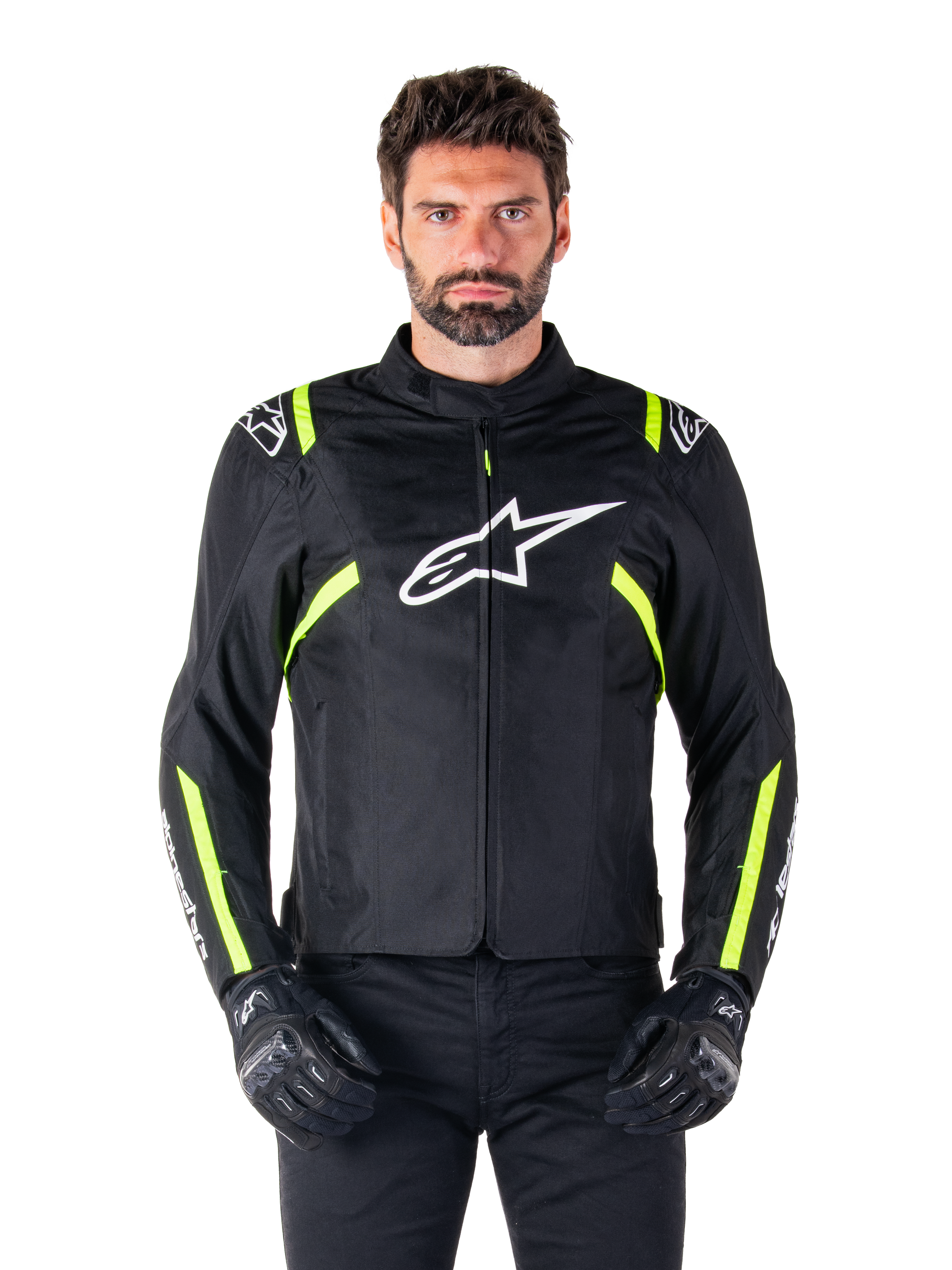 Alpinestars T-SPS V2 Waterproof Jacket, chaqueta de moto, negra con detalles en blanco y amarillo flúor, usada por un modelo con guantes negros, con el logo de la estrella blanca en el pecho y franjas amarillo neón en las mangas y hombros, equipamiento textil deportivo para cualquier clima