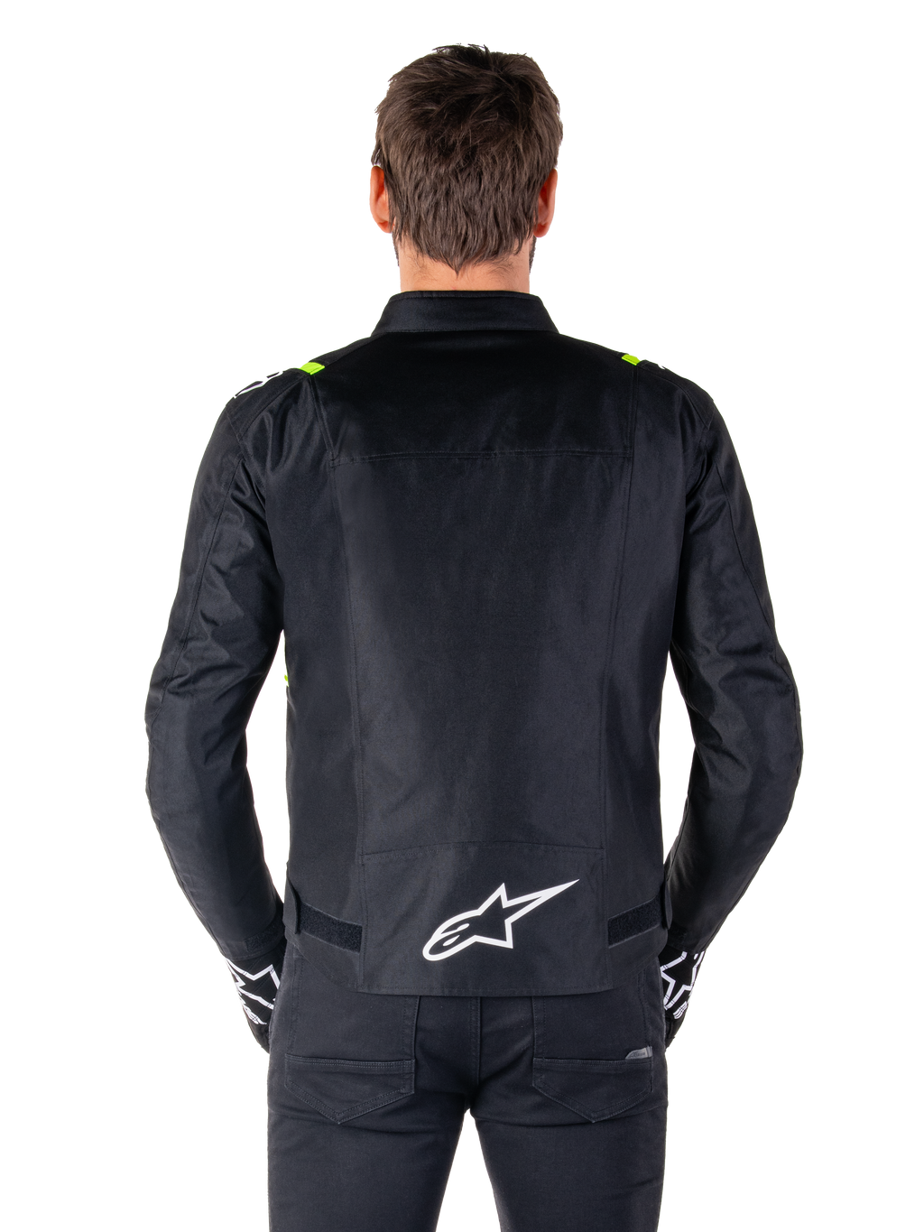 Chaqueta impermeable Alpinestars T-SPS V2, vista posterior, negra con detalles en amarillo flúor en los hombros y logotipo de estrella blanco en la parte inferior de la espalda, chaqueta de moto textil con silueta deportiva, usada por un modelo masculino.