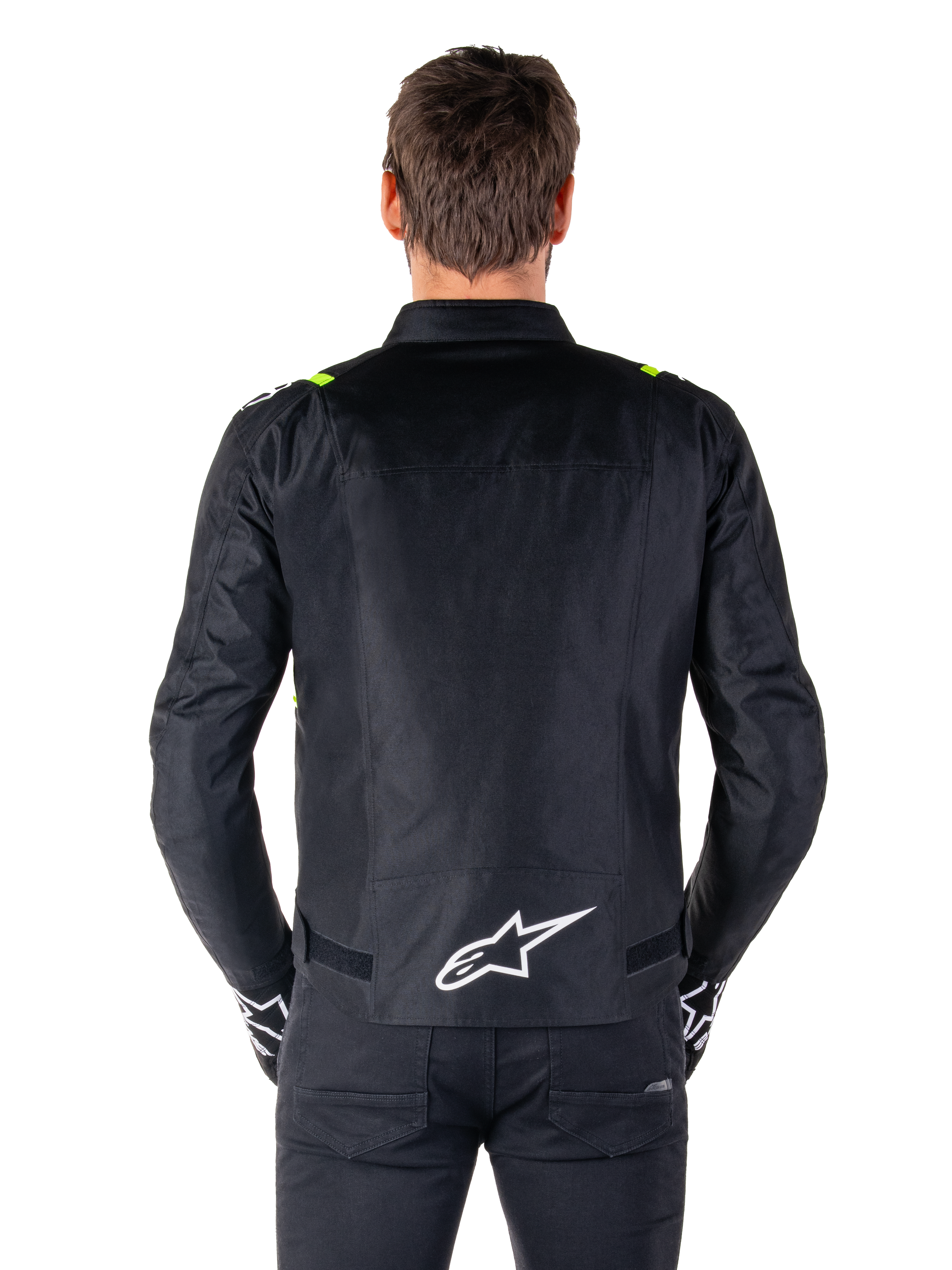 Chaqueta impermeable Alpinestars T-SPS V2, vista posterior, negra con detalles en amarillo flúor en los hombros y logotipo de estrella blanco en la parte inferior de la espalda, chaqueta de moto textil con silueta deportiva, usada por un modelo masculino.