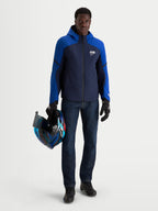 Alpinestars Aeroshell WP Chaqueta, chaqueta de moto softshell impermeable para hombre en azul marino y azul brillante con capucha, usada por un modelo que sostiene un casco a juego