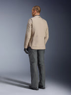 Chaqueta Alpinestars Borrego Drystar® en color Warm Gray, vista trasera que muestra la textura de lona encerada robusta, los paneles de expansión traseros en los hombros y el bolsillo trasero grande con cremallera, lucida por un modelo con pantalones de aventura gris carbón y guantes negros.