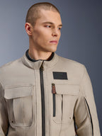 Modelo masculino con la chaqueta Alpinestars Borrego Drystar® en Warm Gray, chaqueta de moto de aventura con un aspecto clásico de lona encerada, bolsillos de carga funcionales en el pecho y un parche negro con el logo de Alpinestars.