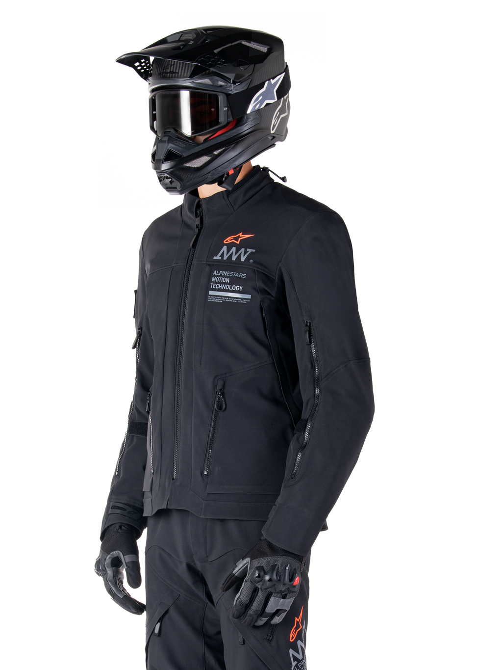 Chaqueta Alpinestars AMT-8 Stretch Drystar® XF, negra, usada por un piloto con pantalones de aventura y guantes a juego, con un casco de motocross negro y gafas, puertos de ventilación con cremallera en el pecho y los brazos, marca Alpinestars Motion Technology con un logotipo naranja, equipamiento premium de turismo de aventura