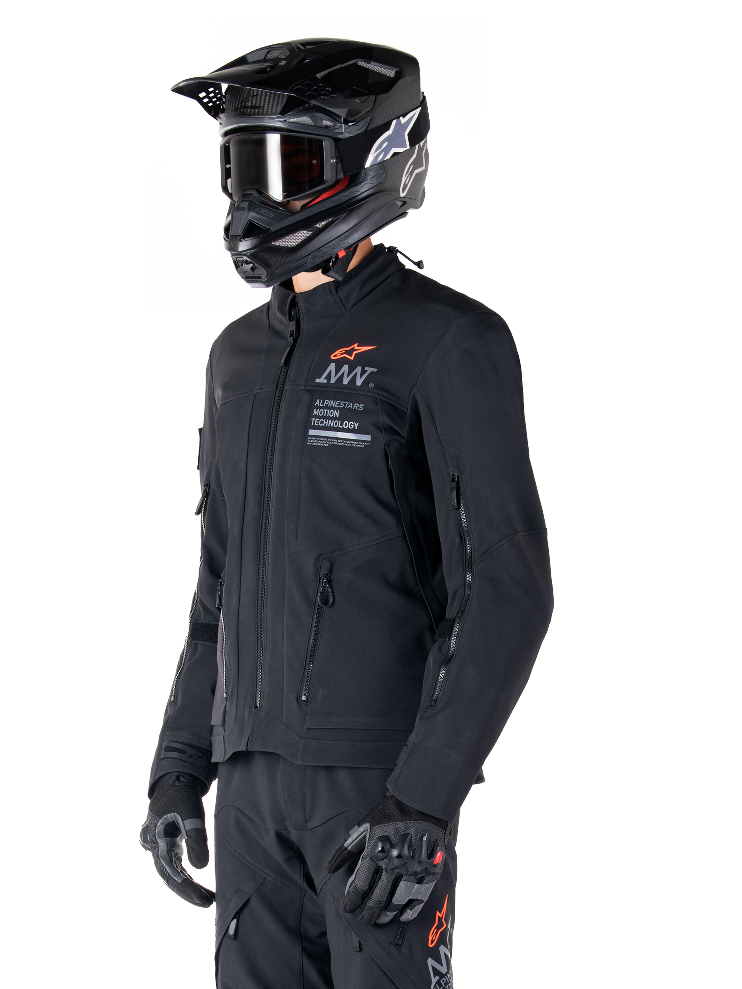 Chaqueta Alpinestars AMT-8 Stretch Drystar® XF, negra, usada por un piloto con pantalones de aventura y guantes a juego, con un casco de motocross negro y gafas, puertos de ventilación con cremallera en el pecho y los brazos, marca Alpinestars Motion Technology con un logotipo naranja, equipamiento premium de turismo de aventura