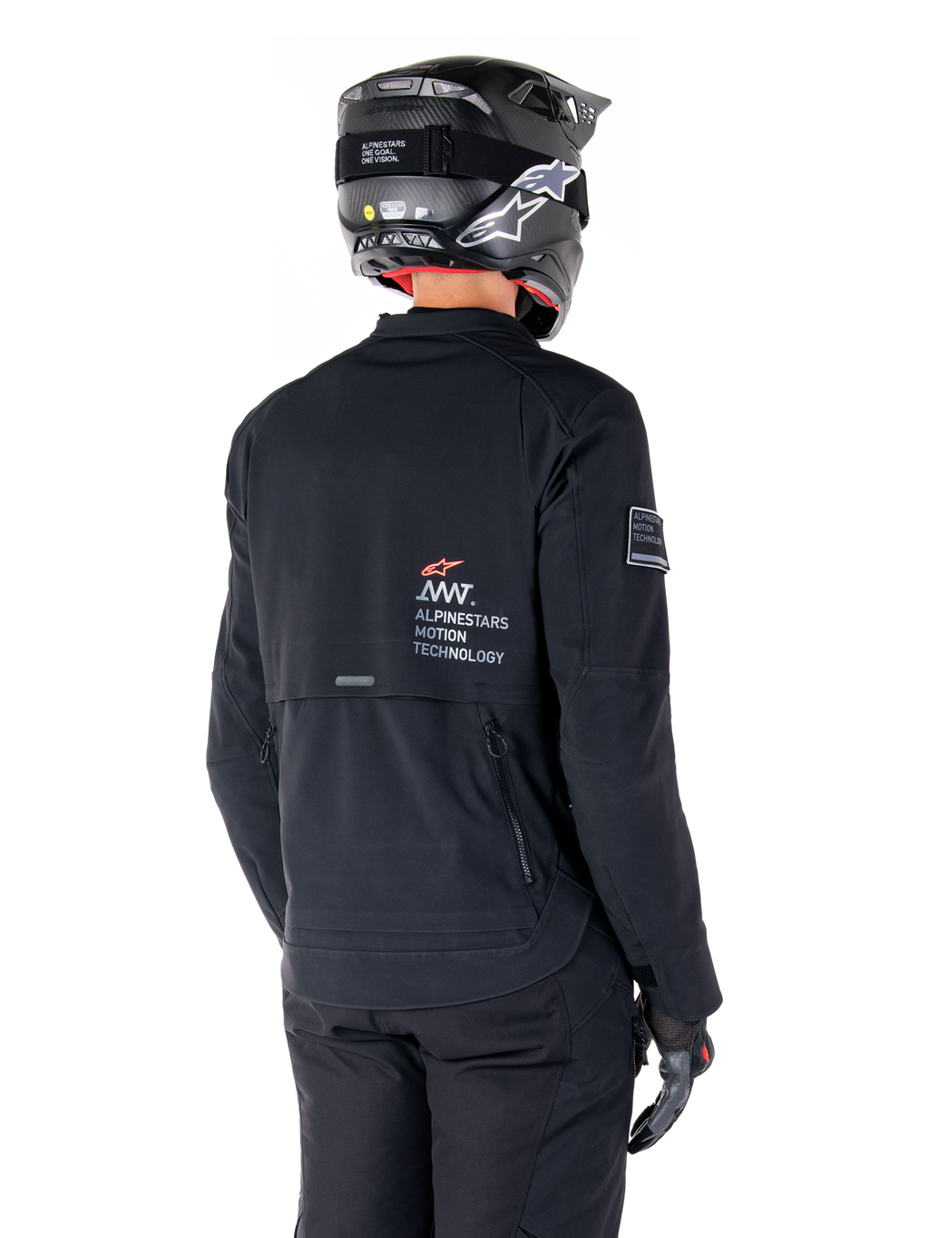 Vista trasera de un piloto con la chaqueta Alpinestars AMT-8 Stretch Drystar® XF en negro, con el logotipo 'AMT Alpinestars Motion Technology' en la espalda y ventilación técnica con cremallera, combinada con casco y guantes de moto negros